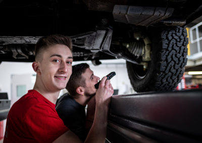 Ein junger Mechaniker in einer Werkstatt kontrolliert einen PKW